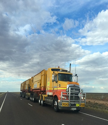 Large yellow semi-truck with vast blue sky and clouds above.