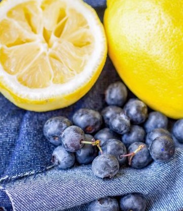 Half of a lemon, one whole lemon and blueberries on jean fabric background