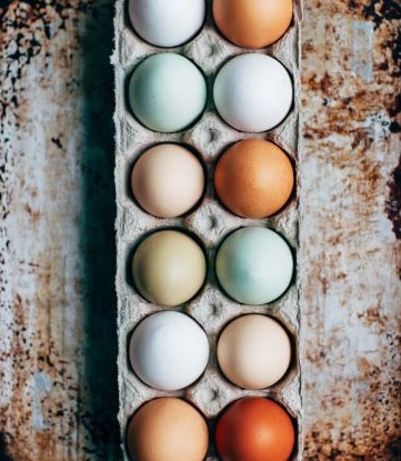 A dozen multi-colored eggs in container on painted table