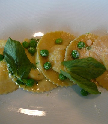 Ravioli with basil and peas on a white plate.