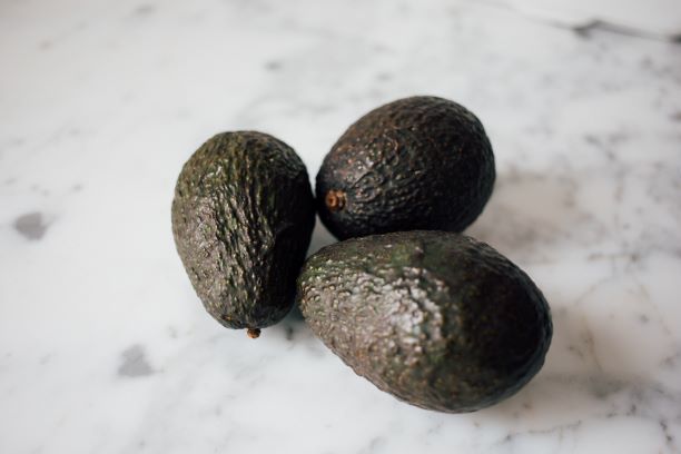 Three avocados on white marble