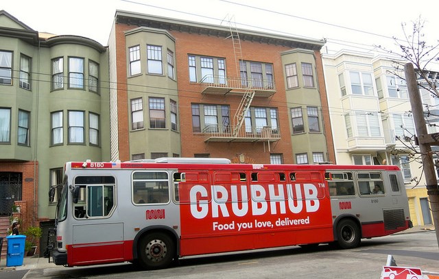 Bus with Grubhub advertising parked in front of apartment buildings.