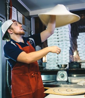 Man throwing pizza dough in air.