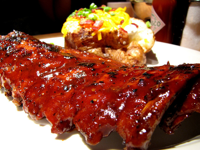 Plate with bbq ribs and baked potato topped with sour cream, cheddar, bacon and green onions