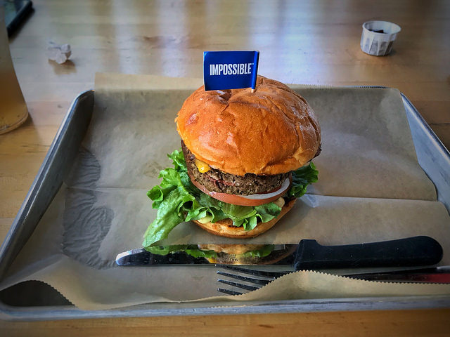 Impossible burger in bun with lettuce and onions on a tray and blue paper flag labeled "impossible"