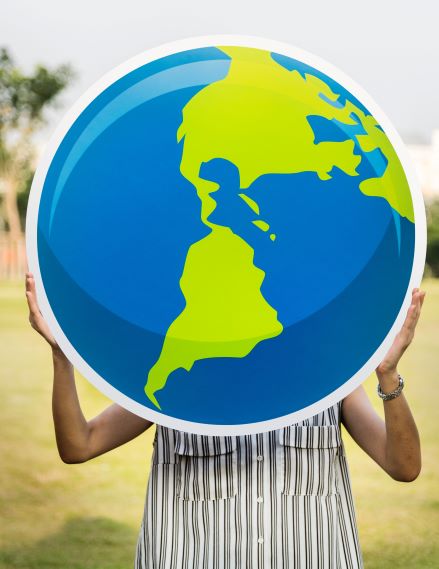 Person in a striped shirt holding cardboard green and blue cutout of earth over face