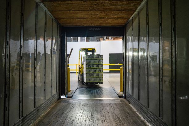 Person driving forklift with boxes in what looks like a refrigerator warehouse