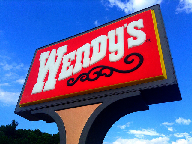 Red and white Wendy's sign against bright blue sky.