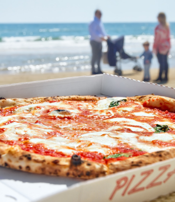 Supply Chain Scene, image of a box of pizza at the beach with family in the background 