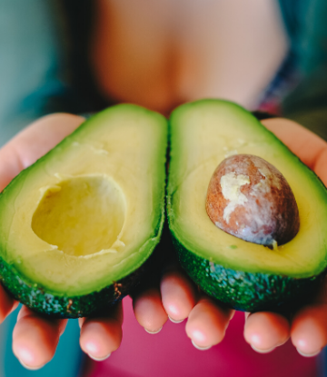 SCS, image of a fresh avocado sliced in half, held in persons hands 