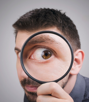 SCS, image of a man hlding a magnifying glass to his eye 