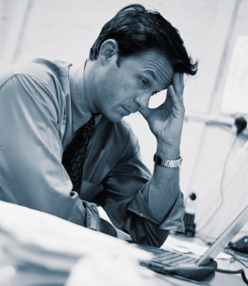 Iamage of very worried man at desk, head in hand 