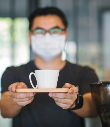 SCS, image of a masked man with arms outstretched, handing a cup of coffee 