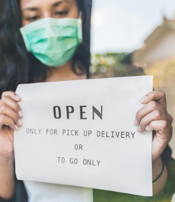Photo of masked woman holding a sign that say open for takeout and delivery only 