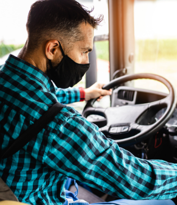 Image of a younger truck driver inside the cab wearing a mask 